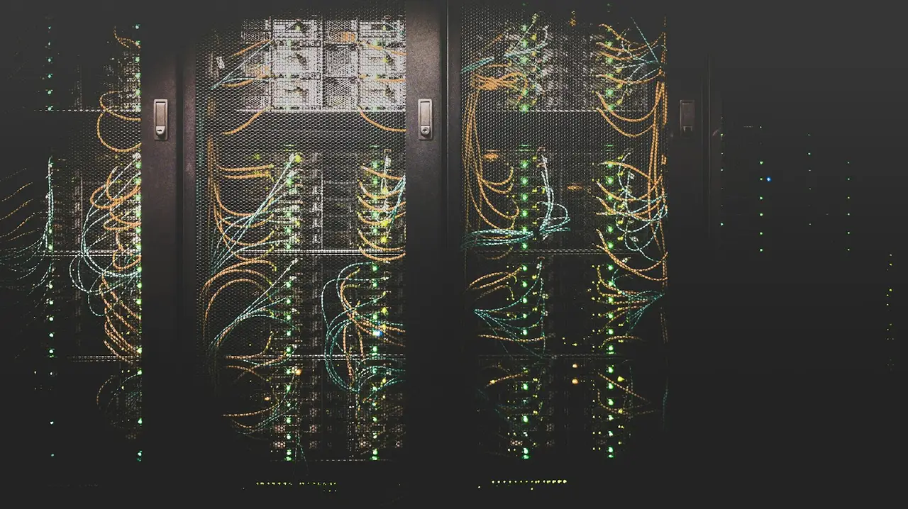 Data center aisle with illuminated server cabinets and cable bundles visible through mesh doors