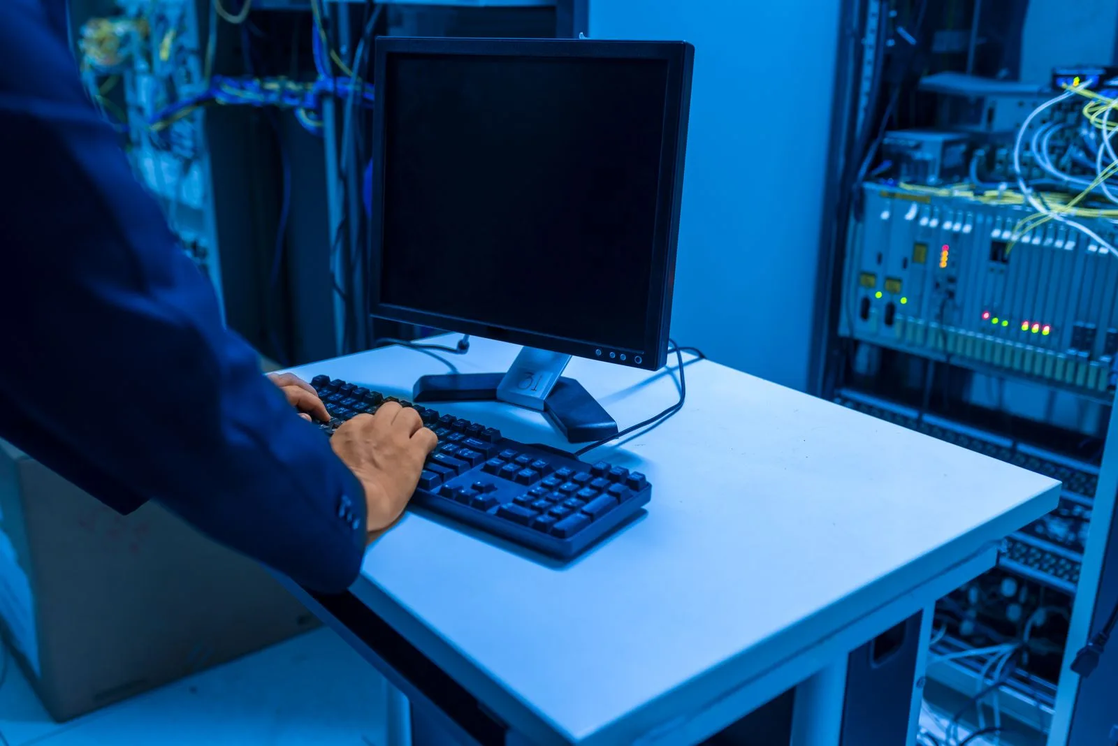 Technician working at a monitor and keyboard beside server equipment